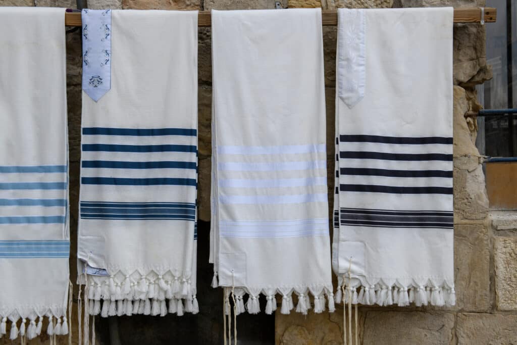 Plain white and striped tallit or tallis (plural tallisim), Jewish prayer shawls, neatly hanging on a display rack outside a Judaica store in Jerusalem, Israel.