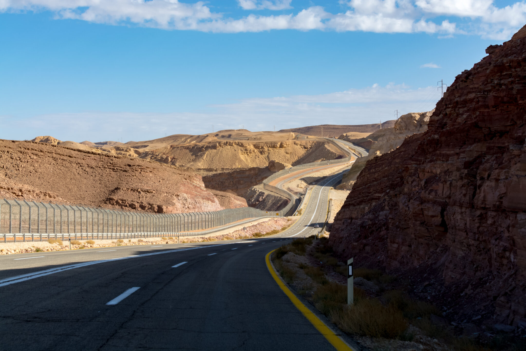 Asphalt road and fence wall on boarder with Egypt in desert Negev
