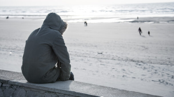 Man staring reflectively at the beach, evocative of mental health issues