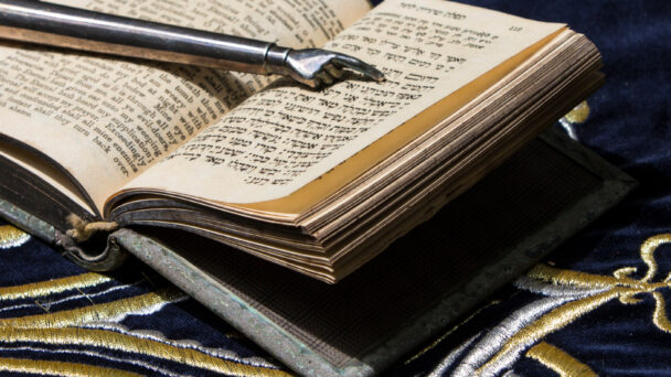 Open bible book in Hebrew with silver pointing hand